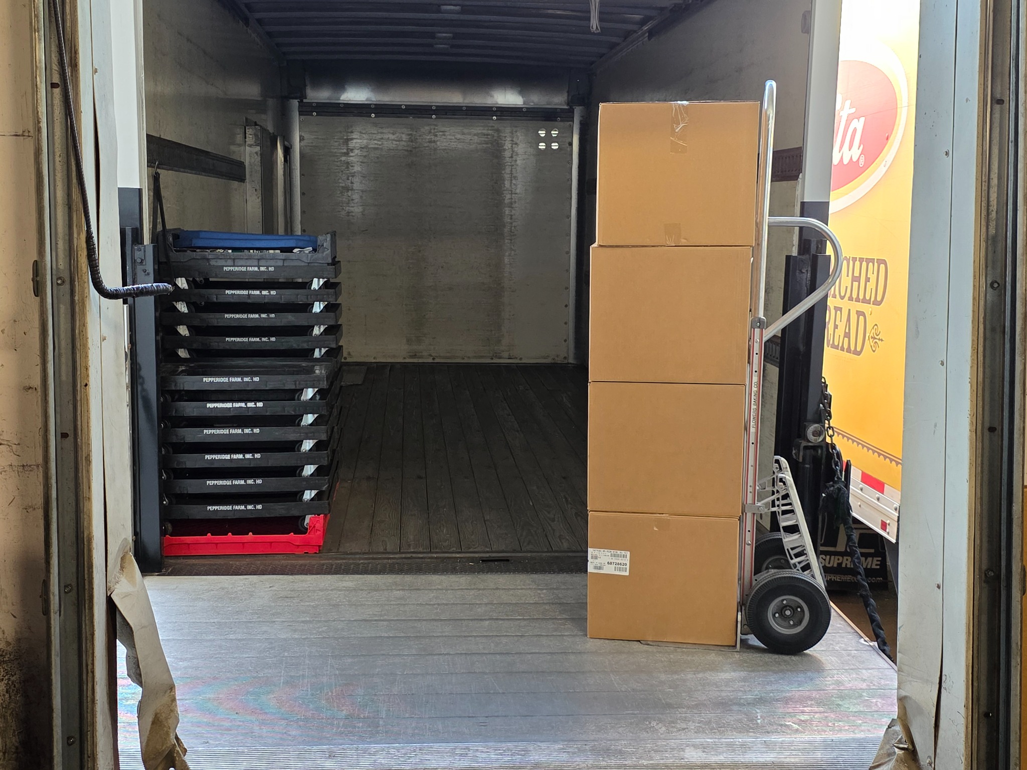 Open delivery truck at the Greenville loading area with boxes, a hand truck, and bread trays